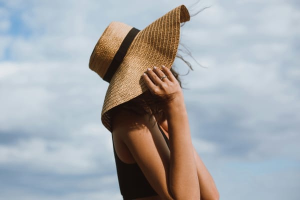 A woman holds onto her wide-brimmed hat while standing in the sun.