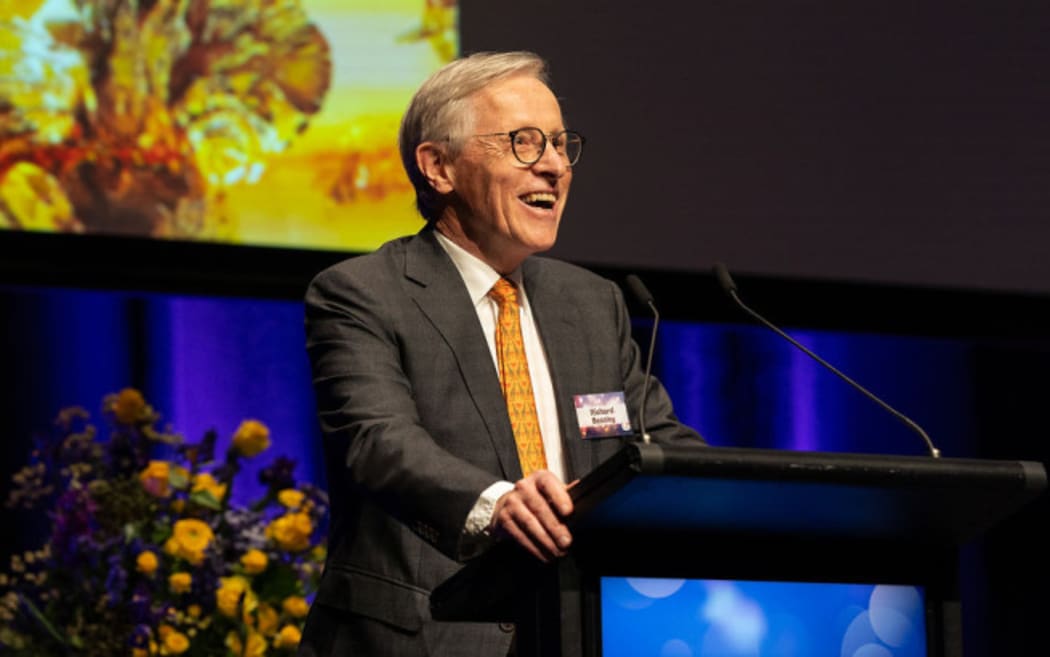 Professor Richard Beasley stands at a podium smiling.