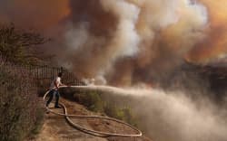 A resident attempts to protect his property from the flames closing in on homes threatened by the wind-driven Palisades Fire in Pacific Palisades, California, January 7, 2025. - A fast-moving brushfire in a Los Angeles suburb burned buildings and sparked evacuations Tuesday as “life threatening” winds whipped the region. More than 200 acres (80 hectares) was burning in Pacific Palisades, a upscale spot with multi-million dollar homes in the Santa Monica Mountains, shuttering a key highway and blanketing the area with thick smoke. (Photo by David Swanson / AFP)