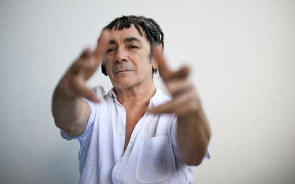 Singer Mark Williams gestures at the camera, wearing a white shirt.