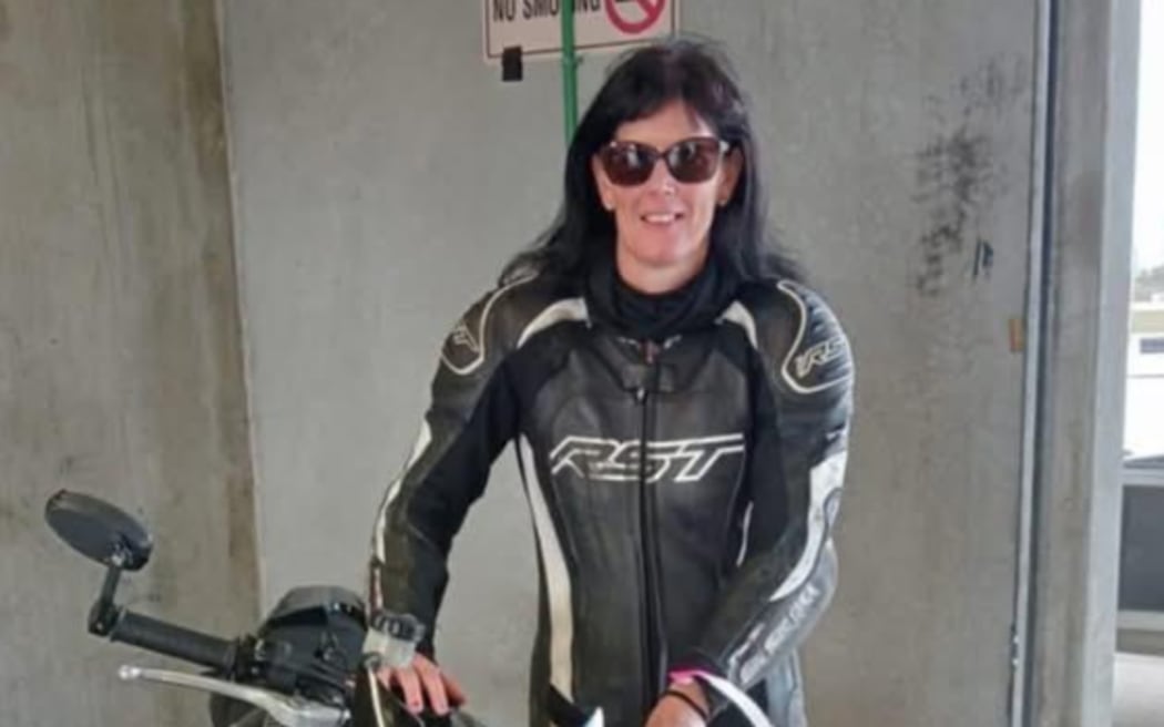 Lesley Brooks poses for a photo with her motorbike in what appears to be a carpark garage. She has long black hair and is wearing sunglasses.