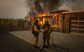 Firefighters discuss how to approach the scene as a home burns near grape vines during the Kincade fire in Healdsburg, California.