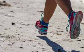 A pair of legs in running shoes move along a beach.