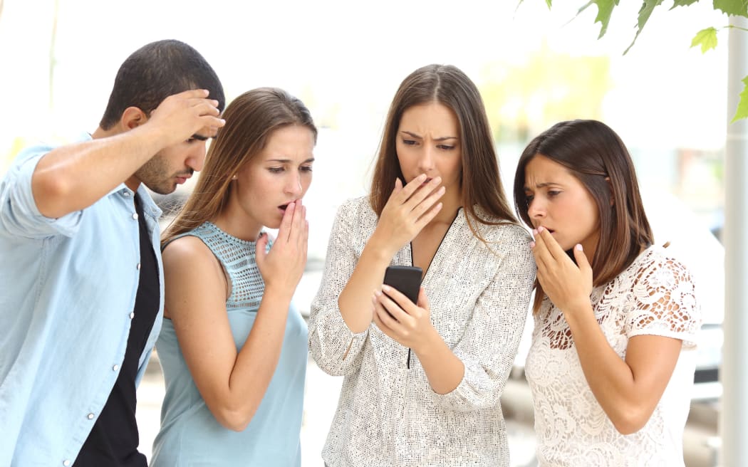 A photo of four worried multi ethnic friends watching a smart phone in the street