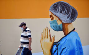 A man wearing face mask walks past a mural depicting of a healthcare worker and a world map with flags on walls of idle cinema building in Mersin, Turkey on June 23, 2020.