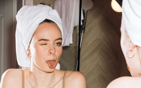 A woman pokes her tongue out in the bathroom window