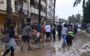 People push shopping carts along a street covered in mud on October 31, 2024 after flash floods ravaged Paiporta, in Valencia, eastern Spain. - Rescuers raced on October 31, 2024 to find survivors and victims of once-in-a-generation floods in Spain that killed at least 95 people and left towns submerged in a muddy deluge with overturned cars scattered in the streets. About 1,000 troops joined police and firefighters in the grim search for bodies in the Valencia region as Spain started three days of mourning. Up to a year's rain fell in a few hours on the eastern city of Valencia and surrounding region on October 29 sending torrents of water and mud through towns and cities. (Photo by JOSE JORDAN / AFP)