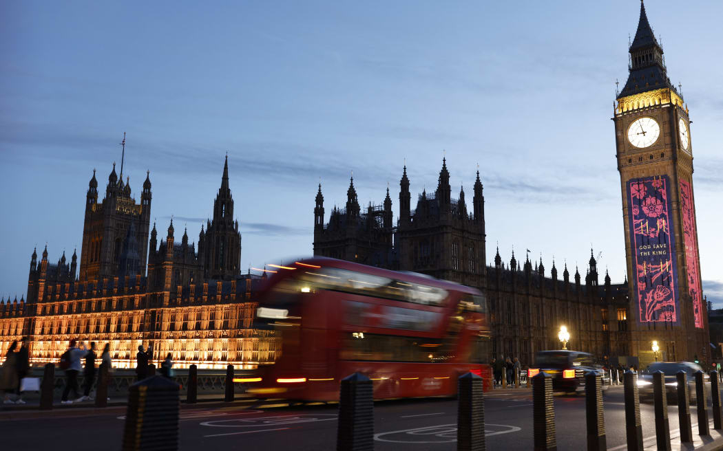 A red London bus passes by as The Elizabeth Tower, commonly known by the name of the clock's bell, "Big Ben" displays a 'God Save the King' projection in central London, on May 4, 2023, ahead of the coronation weekend.