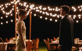 A screenshot from the movie Materialists. Two actors look at each other across a night-time garden party scene.