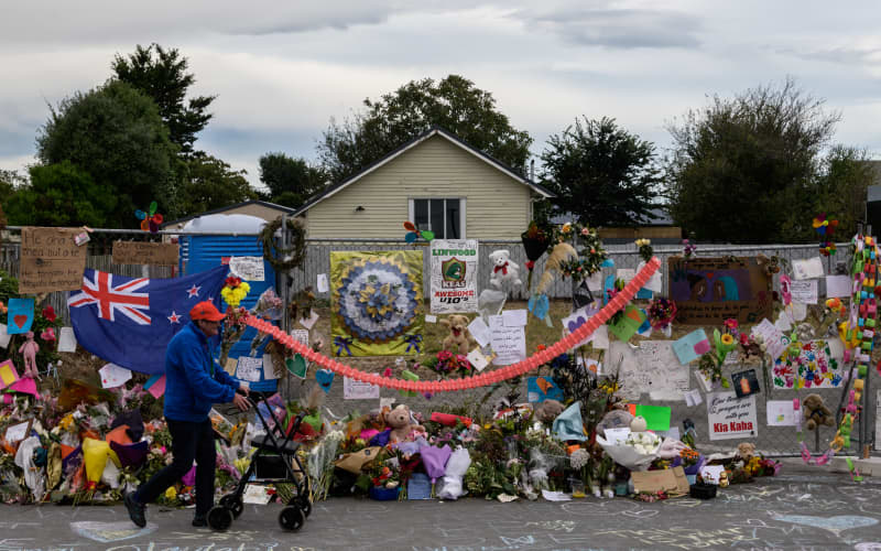 A man man walks past flowers and tributes displayed in memory of the twin mosque massacre victims along the road outside the Linwood mosque (back C) in Christchurch on March 25, 2019. The slaughter of 50 people at Friday prayers in two Christchurch mosques on March 15 shocked the normally laid-back country and prompted global horror, heightened by the gunman’s cold-blooded livestreaming of the massacre. (Photo by ANTHONY WALLACE / AFP)