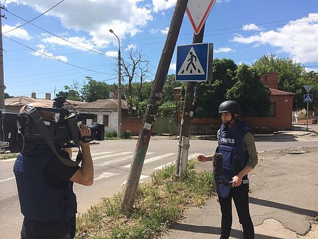 Kim Vinnell in flak jacket and helmet facing TV camera on street in Mariupol Uklraine