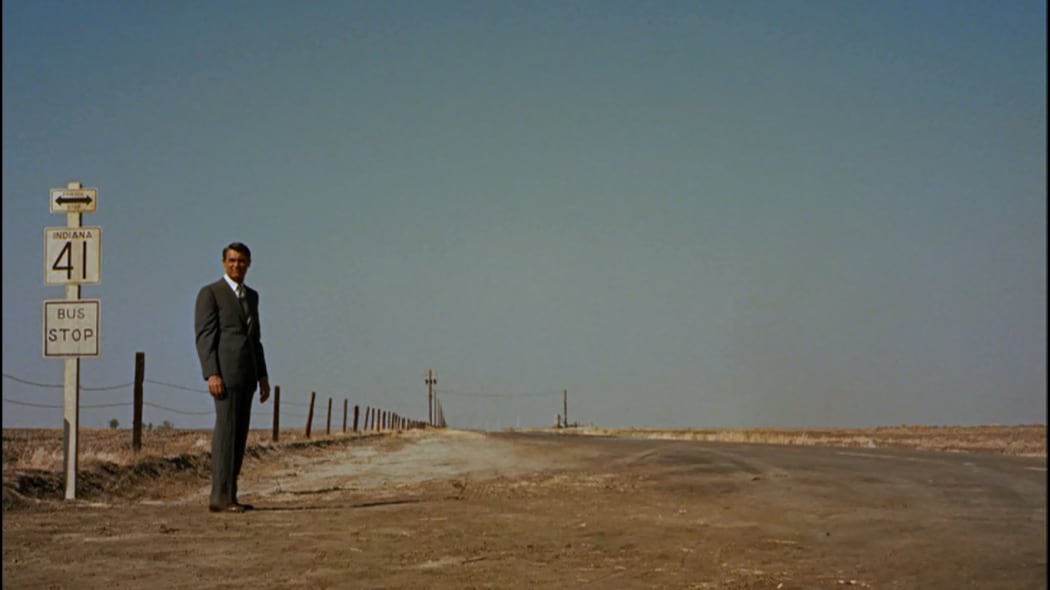 Movie still from Alfred Hitchcock's 1959 film North by Northwest depicting Cary Grand as Roger Thornhill waiting for a bus in an Indiana cornfield.