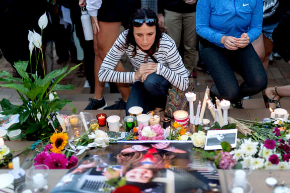 A woman kneels next to candles and flowers near a photo of British backpacker Grace Millane during the vigil at Civic Square Park in Wellington.