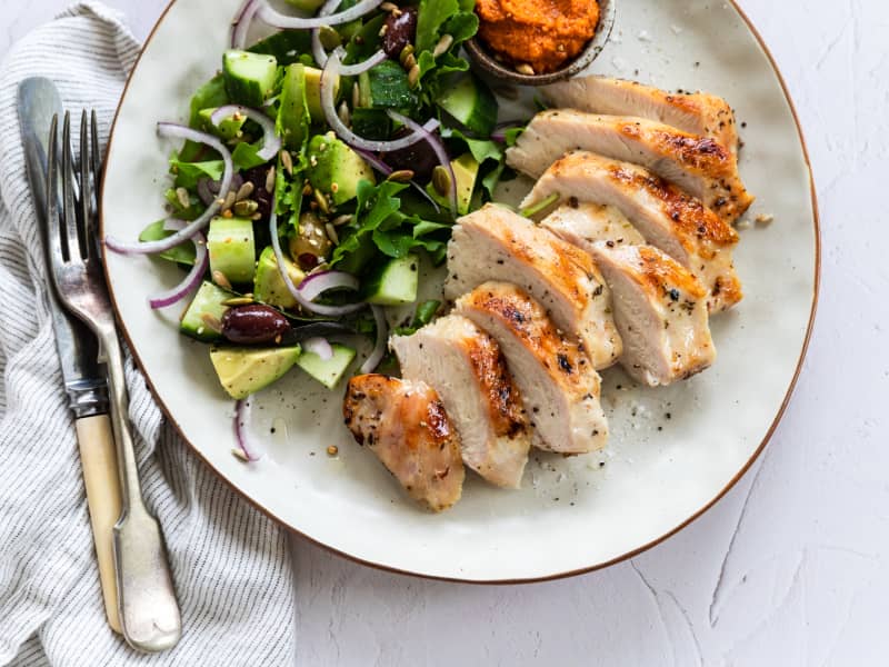 A plate showing some sliced brined and barbequed chicken breasts alongside a salad of lettuce, avocado and red onion.
