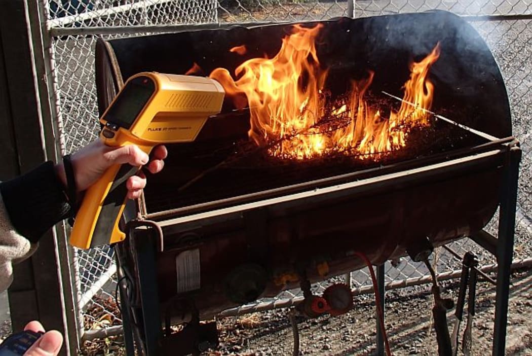 A laser thermometer reads the temperature as samples of plants are incinerated on the plant barbecue.