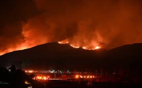Fire trucks and public security vehicles are seen in the foreground as red glowing flames and smoke rise from the Hughes Fire in Castaic in northwest Los Angeles County, California, on January 22, 2025. A new wildfire erupted north of Los Angeles on January 22, exploding in size and sparking thousands of evacuation orders in a region already staggering from the effects of huge blazes. Ferocious flames were devouring hillsides near Castaic Lake, spreading rapidly to cover 5,000 acres (2,000 hectares) in just over two hours.