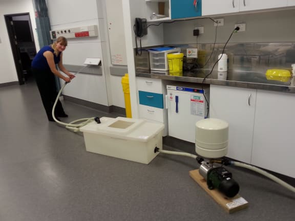 A photo of Susann Beier with the pipes and flow pump for the bloodlike fluid outside the MRI room