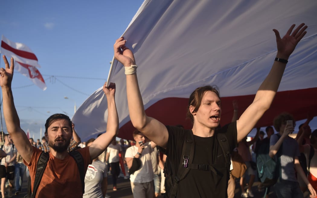 Belarus opposition supporters hold a giant former white-red-white flag of Belarus used in opposition to the government, during a demonstration in central Minsk on August 16, 2020.