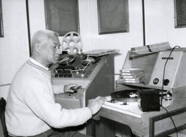 A white-haired man sits in front of recording equipment.