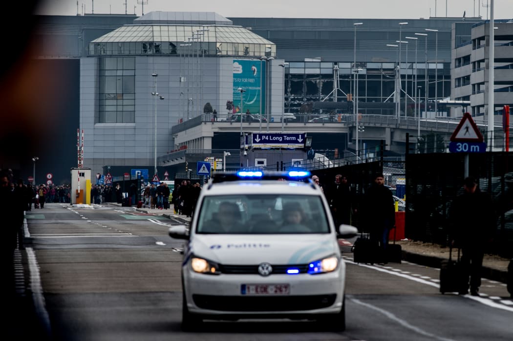 A Belgian police vehicle driving past passengers who are evacuating the Brussels Airport of Zaventem.