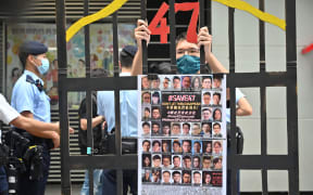 A protester stands behind a mock jail with photos of the 47 pro-democracy figures already in prison as Hong Kong's political elite on September 19, 2021 began selecting a powerful commmittee which will choose the city's next leader and nearly half the city's legislature under a new "patriots only" system imposed by Beijing. Hong Kong's Court of Appeal upheld the jailing of 12 democracy campaigners on February 23, 2026 as part of a high-profile subversion case under a Beijing-imposed national security law. (Photo by Peter PARKS / AFP)