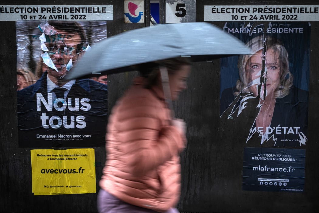 A pedestrian walks past campaign poster of French President Emmanuel Macron and presidential candidate Marine Le Pen of the far-right Rassemblement National party.