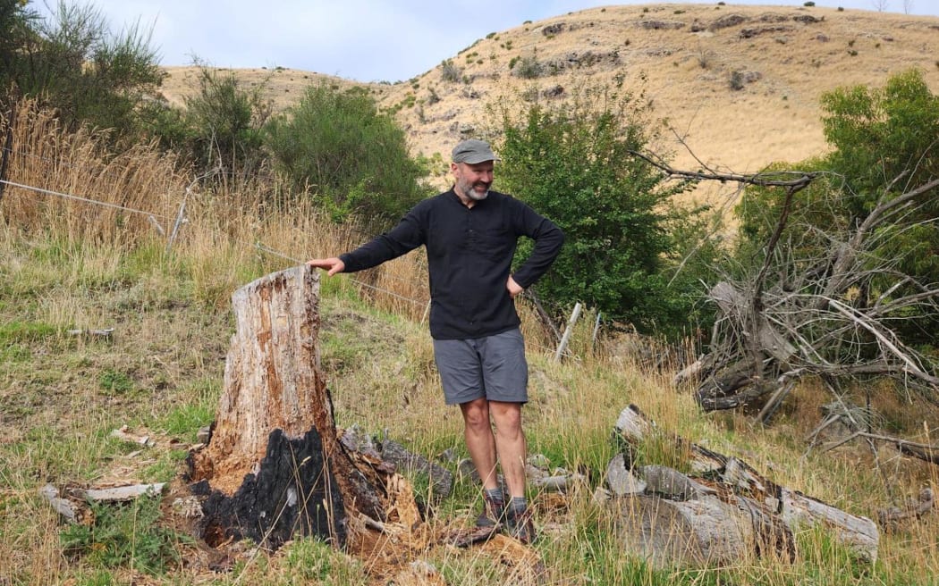 Port Hills resident and senior University of Canterbury Environment lecturer Matiu Prebble stands next to a scorched stump from the 2017 fires, about 100 meters from his home.