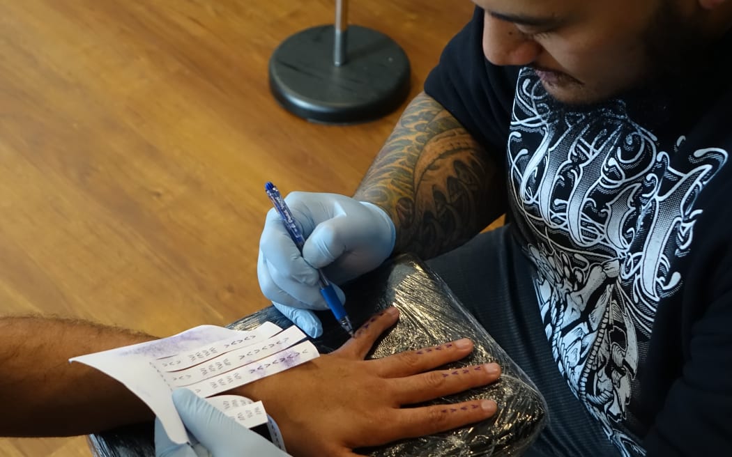 Tattoo artist Chris Amosa preparing to tattoo a design by Vaimaila Urale as part of the 'Typeface' live tattoo session for the Avondale Whau Arts Festival.