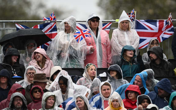 Members of the public cover themselves against the rain as they wait for the return of Britain's King Charles III and Britain's Camilla, Queen Consort outside Buckingham Palace, in central London, on May 6, 2023 ahead of their coronations. - The set-piece coronation is the first in Britain in 70 years, and only the second in history to be televised. Charles will be the 40th reigning monarch to be crowned at the central London church since King William I in 1066. (Photo by Marco BERTORELLO / AFP)