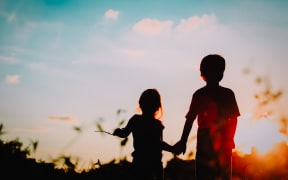 little boy and girl silhouettes holding hands at sunset nature