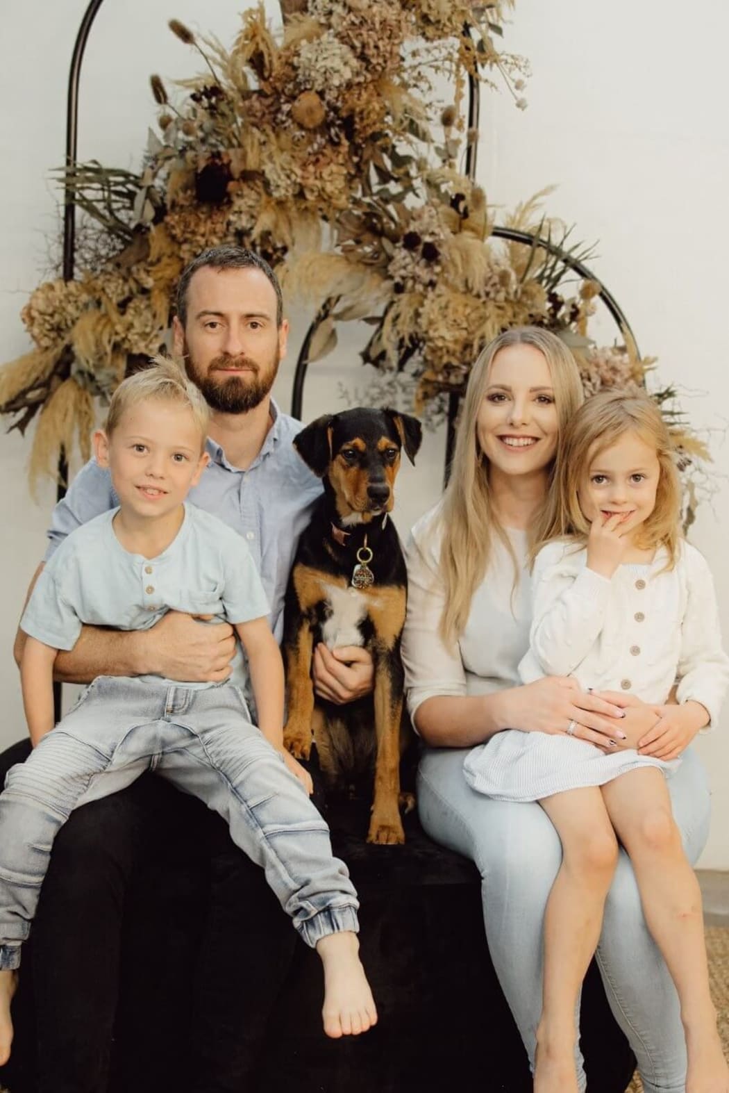 A family portrait. Mum Fallon and Dad Tom sit with their two kids on their knees, and their dog in between them. They all smile at the camera.
