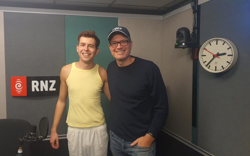 Jesse Mulligan and James Mustapic in the RNZ Auckland studio. James wears a yellow singlet. Jesse is wearing a Fly DC3 cap.