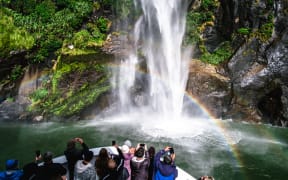 A group of tourists enjoying a stunning scene of nature while cruising into waterfall in Milford Sound, New Zealand.