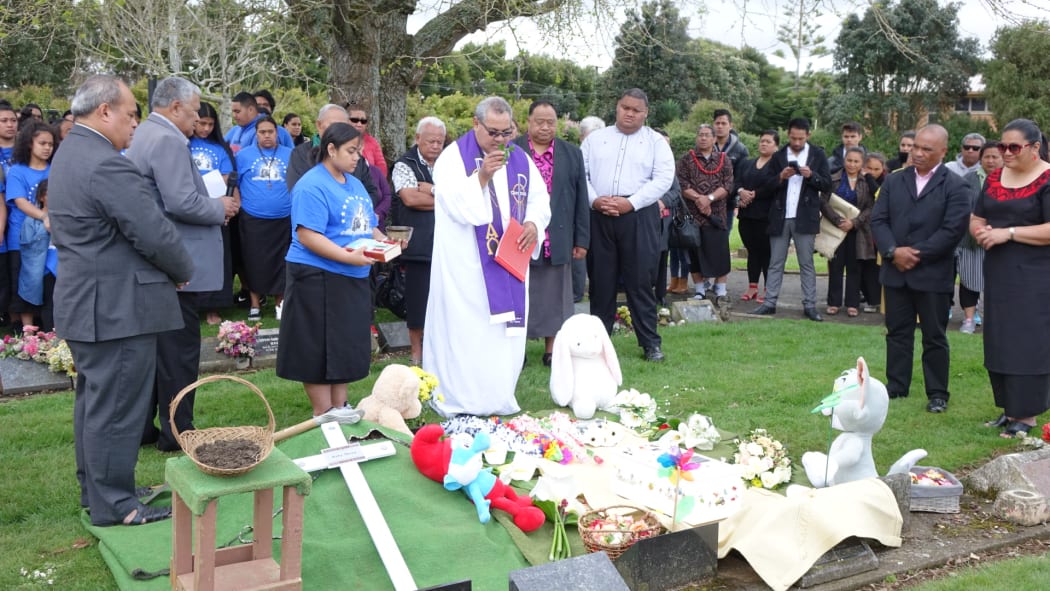 A priest blesses the grave of baby Mona.