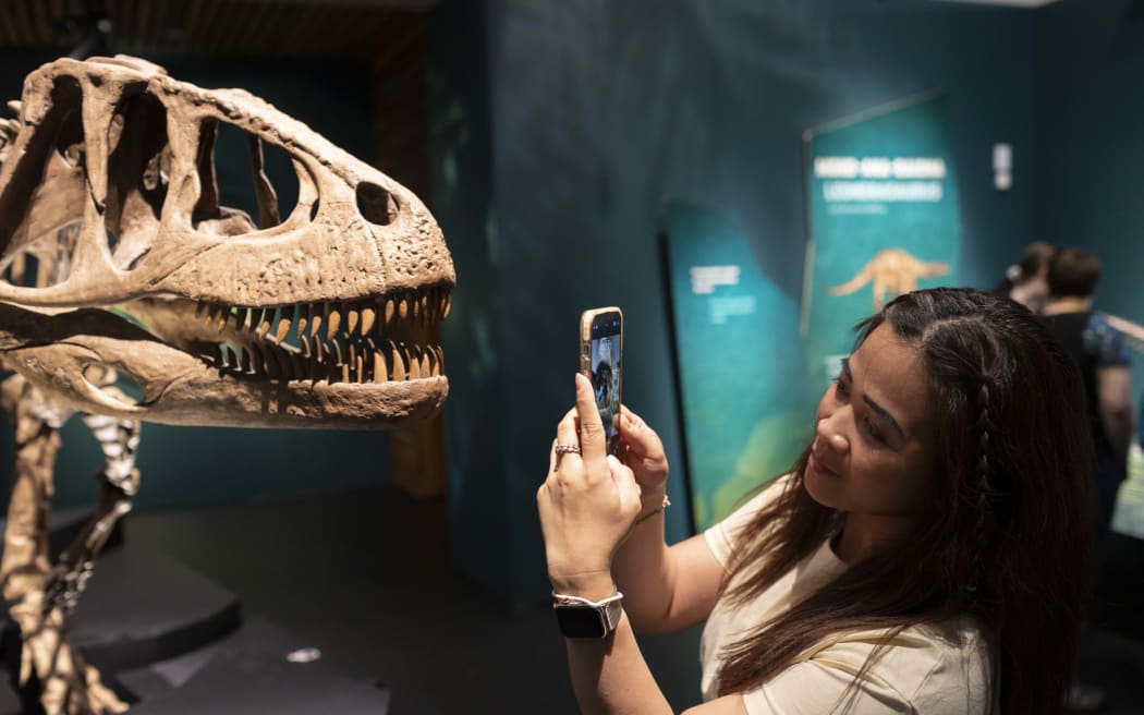A girl holds a smartphone up to the sharp teeth of a dinosaur skeleton.
