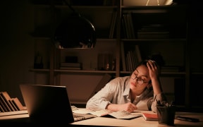A picture of a woman who is working late at night, in front of a laptop, and exhausted.