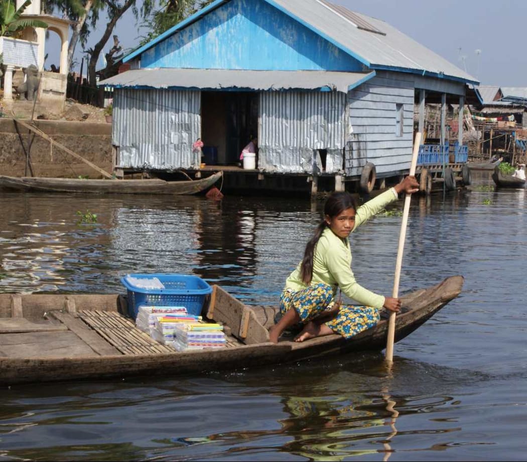 Young girl in Cambodia in canoe in front of over water tin shacks