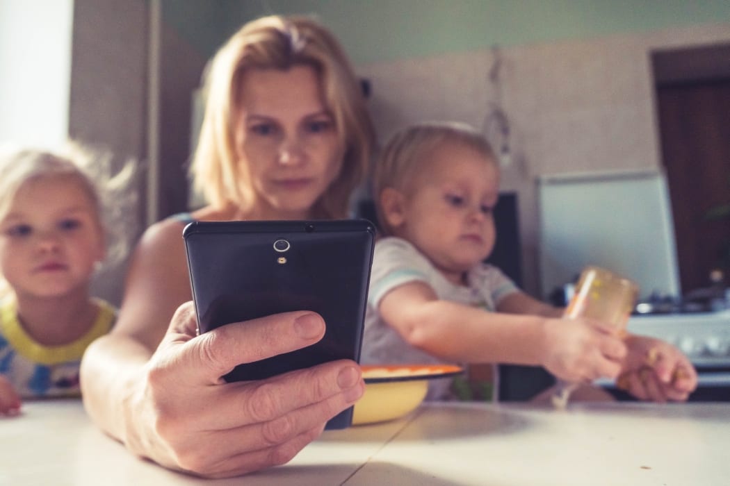 mother looking at mobile phone while with two children