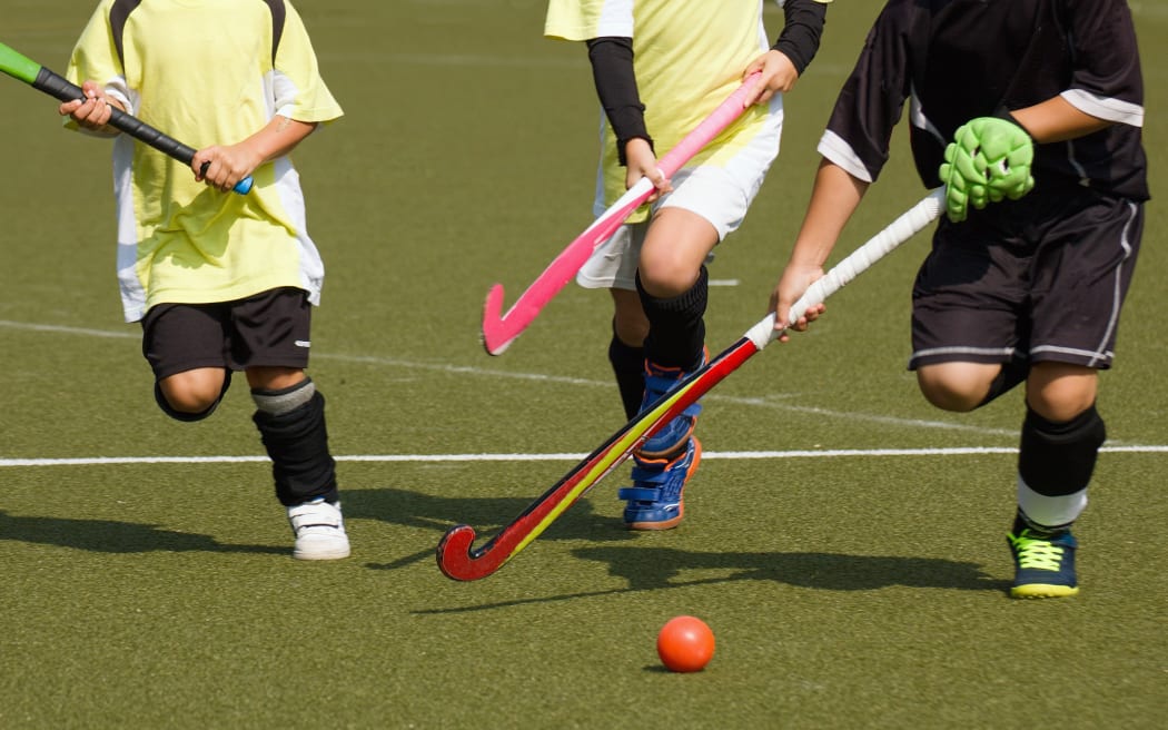 Children playing field hockey competitively. Two teammates in yellow jerseys chase running player in black uniform
