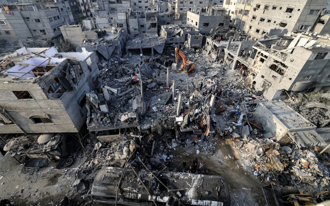 An excavator clears rubble as people search for survivors and the bodies of victims through buildings that were destroyed during Israeli bombardment in Khan Yunis in the southern Gaza Strip on 25 October 2023, amid the ongoing battles between Israel and the Palestinian group Hamas.