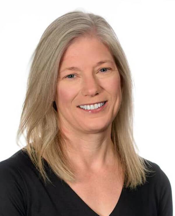 Devoney Looser is a smiling woman in a black top with long blonde hair.