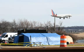An American Eagle plane lands at Reagan National Airport as investigators use a temporary shed to gather pieces of wreckage after American Airlines flight 5342 on approach to the airport collided with a US Army helicopter, near Washington, DC, on January 30, 2025. There are likely no survivors from a collision between a passenger jet and US Army helicopter in Washington, officials said Thursday, as recovery operations pulled 28 bodies from the river into which both crashed.