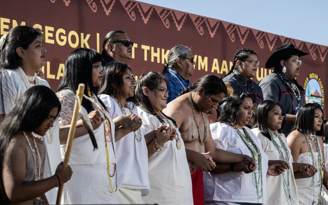 Members of the indigenous community sing after US President Joe Biden speaks at the Gila River Crossing school, to apologize to Indigenous communities for boarding schools that separated families, in Laveen Village, Arizona on October 25, 2024. - Biden apologized for one of the country's "darkest chapters:" the abduction of Native American children from their families and placement in abusive boarding schools aimed at erasing their culture. The first public apology issued by a sitting US president. From the early 1800s until the 1970s, the US ran hundreds of Indian boarding schools across the country to forcibly assimilate Native children into European settler culture, including conversion to Christianity. (Photo by ANDREW CABALLERO-REYNOLDS / AFP)