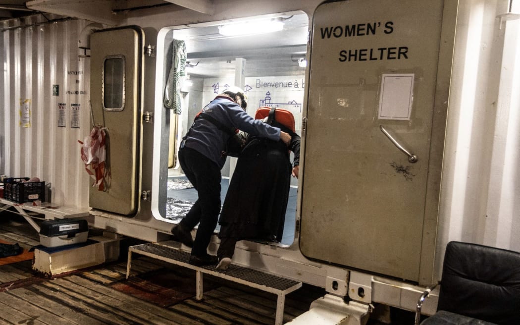 This photo taken on March 13, 2024 and handout on March 14, 2024 by international humanitarian organization SOS Mediterranee, shows a volunteer (L) helping a rescued migrant enter the "Women's Shelter", a room dedicated to women aboard the Ocean Viking rescue vessel, following a rescuing operation of migrants in the Libyan search and rescue region in international waters. The Ocean Viking migrant rescue vessel chartered by SOS Mediterranee rescued 25 people off the coast of Libya on March 13, 2024, who had been in "an inflatable boat adrift" for "around a week", the NGO said in a press release. "Those rescued report that many people have died and are now missing", said SOS Mediterranee. (Photo by Johanna de TESSIERES / SOS MEDITERRANEE / AFP) / RESTRICTED TO EDITORIAL USE - MANDATORY CREDIT "AFP PHOTO / HO / JOHANNA de TESSIERES / SOS MEDITERRANEE   " - NO MARKETING NO ADVERTISING CAMPAIGNS - DISTRIBUTED AS A SERVICE TO CLIENTS
