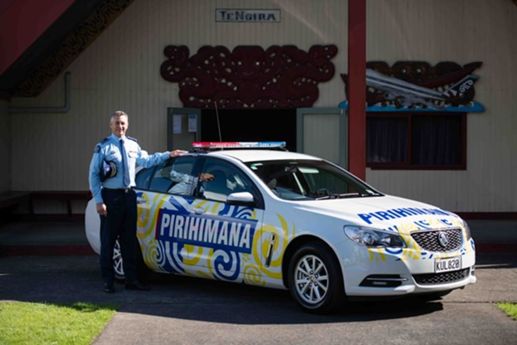 Police Commissioner Mike Bush stands next to the car featuring koru designs and te reo Māori.