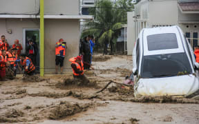 Rescuers wade through flood waters by holding a rope in their effort to evacuate residents who are trapped at their houses in Padang, West Sumatra province on November 27, 2025. (Photo by REZAN SOLEH / AFP)