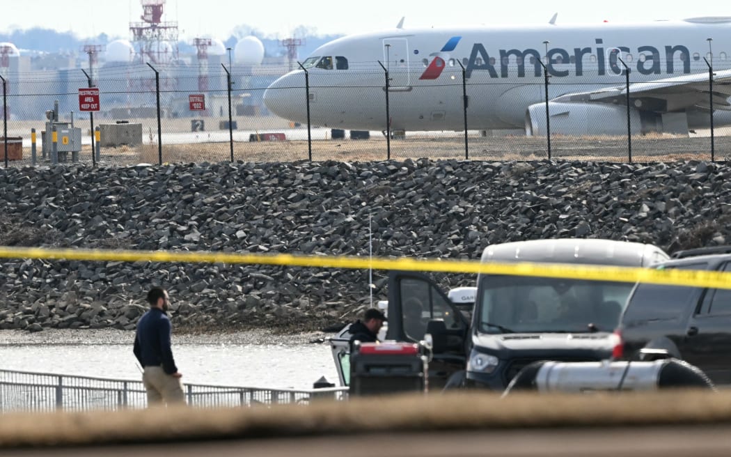 An American Airlines plane prepares to take off as investigators carry pieces of wreckage from the waters of the Potomac River after American Airlines flight 5342 on approach to Reagan National Airport crashed into the river after colliding with a US Army helicopter, near Washington, DC, on January 30, 2025. There are likely no survivors from a collision between a passenger jet and US Army helicopter in Washington, officials said Thursday, as recovery operations pulled 28 bodies from the river into which both crashed.
