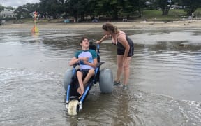 Finlay and Kimberly Graham at Takapuna Beach in Finlay’s community-funded beach wheelchair.