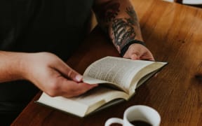 Man with tattoos reading and drinking coffee