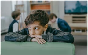 Image of a child looking worried turned away from a television